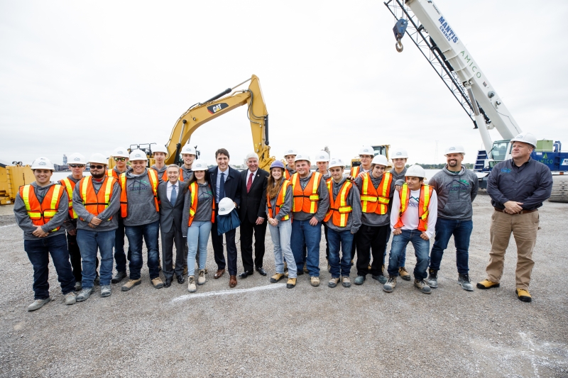 Prime Minister Justin Trudeau, Michigan Governor Rick Snyder and other dignitaries, workers and students standing in front of construction equipment at the Gordie Howe International Bridge construction site. 